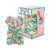 Bear made out of pink, yellow, and green-colored faux marshmallows. The bear is adorned with a green ribbon tied into a bow around its neck, and it is packaged in a clear-front gift box with a pink and white striped design. The top of the box features a teal and pink label that reads "MARSHMALLOW BEAR." This delightful creation is an excellent gift idea for various occasions such as anniversaries, birthdays, graduations, Christmas, Valentine's Day, or simply as a unique gift for someone special.