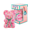 Bear made out of pink, white, peach and pink-colored faux marshmallows. The bear is adorned with a green ribbon tied into a bow around its neck, and it is packaged in a clear-front gift box with a pink and white striped design. The top of the box features a teal and pink label that reads "MARSHMALLOW BEAR." This delightful creation is an excellent gift idea for various occasions such as anniversaries, birthdays, graduations, Christmas, Valentine's Day, or simply as a unique gift for someone special.