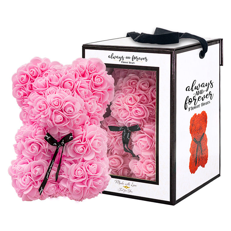 Pink, rose-shaped faux bloom bear with a black ribbon around its neck that includes the text "Just for You". The bear is placed next to a stylish white gift box with black accents, which has a clear window. The box comes with a black carrying handle. This intricately crafted floral bear serves as a perfect gift for various occasions such as anniversaries, birthdays, graduations, Christmas, Valentine's Day, or simply as a beautiful decorative item for those special moments.