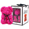 Pink, rose-shaped faux bloom bear with a black ribbon around its neck that includes the text "Just for You". The bear is placed next to a stylish white gift box with black accents, which has a clear window. The box comes with a black carrying handle. This intricately crafted floral bear serves as a perfect gift for various occasions such as anniversaries, birthdays, graduations, Christmas, Valentine's Day, or simply as a beautiful decorative item for those special moments.