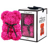 Pink, rose-shaped faux bloom bear with a black ribbon around its neck that includes the text "Just for You". The bear is placed next to a stylish white gift box with black accents, which has a clear window. The box comes with a black carrying handle. This intricately crafted floral bear serves as a perfect gift for various occasions such as anniversaries, birthdays, graduations, Christmas, Valentine's Day, or simply as a beautiful decorative item for those special moments.