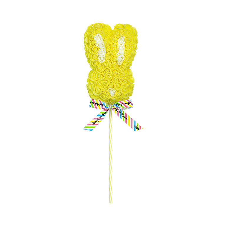 A yellow floral bunny lollipop with a patterned ribbon on a striped stick, featuring a playful arrangement of roses in a bunny shape.
