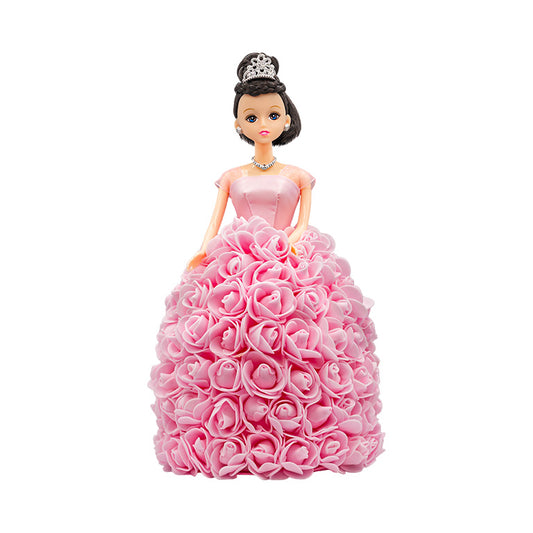 This image showcases a doll with black hair and blue eyes, wearing a light pink gown with a strapless bodice and a full skirt adorned with light pink roses. The doll is embellished with a silver tiara and a complementary necklace.