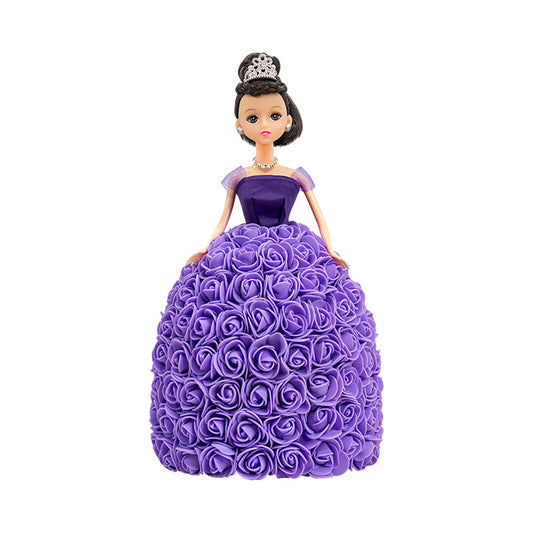 Displayed is a doll with black hair and green eyes, wearing a purple gown with a strapless bodice and a skirt fully covered with purple roses. She is adorned with a silver tiara and a necklace that matches.