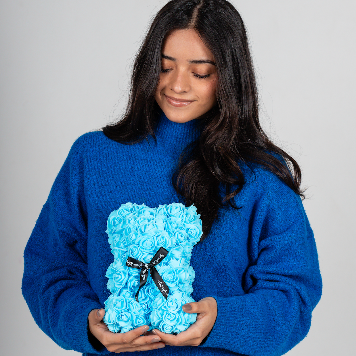 A bear shaped product covered in foam roses in the color blue. Has three pieces of decoration.