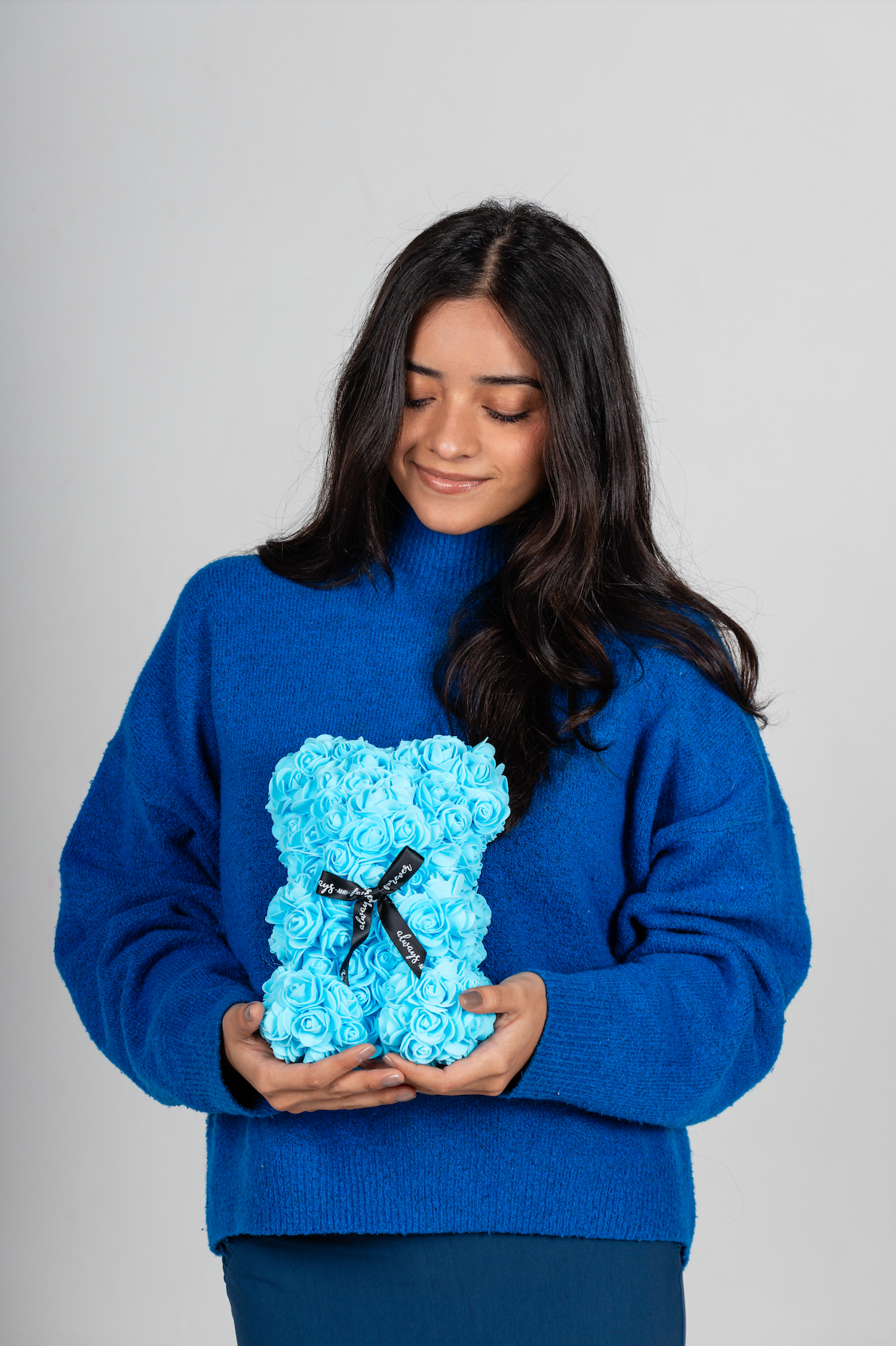 A bear shaped product covered in foam roses in the color blue. Has three pieces of decoration.