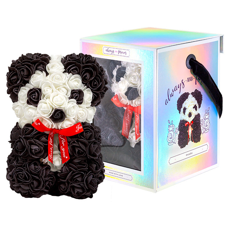 The image shows a black and white artificial flower panda with a heart-shaped arrangement of white flowers for the face and black flowers for the rest of the body. It has a red ribbon bow around the neck with the text "Just for You." The panda is beside its holographic box packaging, which has a transparent window displaying another panda and the text "always and forever" with a "Made with Love" label.