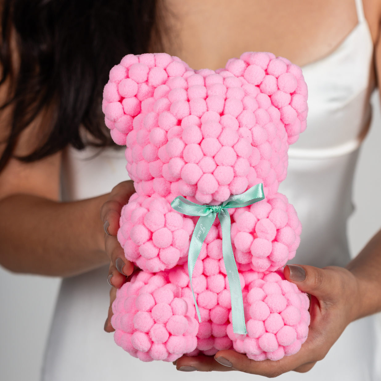 Bear made out of light pink-colored faux marshmallows. The bear is adorned with a green ribbon tied into a bow around its neck, and it is packaged in a clear-front gift box with a pink and white striped design. The top of the box features a teal and pink label that reads "MARSHMALLOW BEAR." This delightful creation is an excellent gift idea for various occasions such as anniversaries, birthdays, graduations, Christmas, Valentine's Day, or simply as a unique gift for someone special.