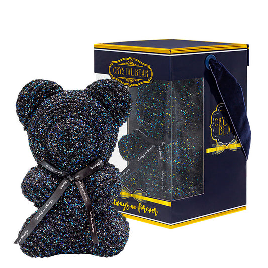 This is a decorative object depicting a bear made of black crystals with multi-colored sparkles. It features a black ribbon around its neck with the text "Always and Forever." The bear is presented in a clear plastic box with a navy blue base and a gold and navy label reading "CRYSTAL BEAR."