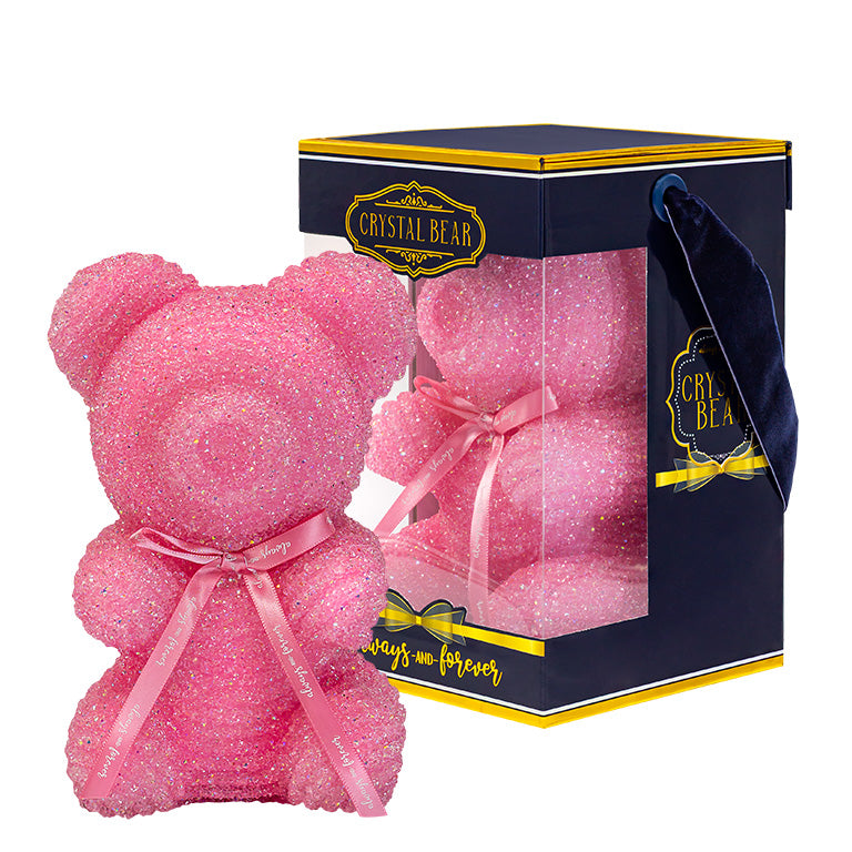 This image shows a sparkling pink crystal bear with a light pink ribbon around its neck that reads "Always and Forever." It's encased in a transparent box with a navy and gold base. The box is adorned with a label stating "CRYSTAL BEAR."