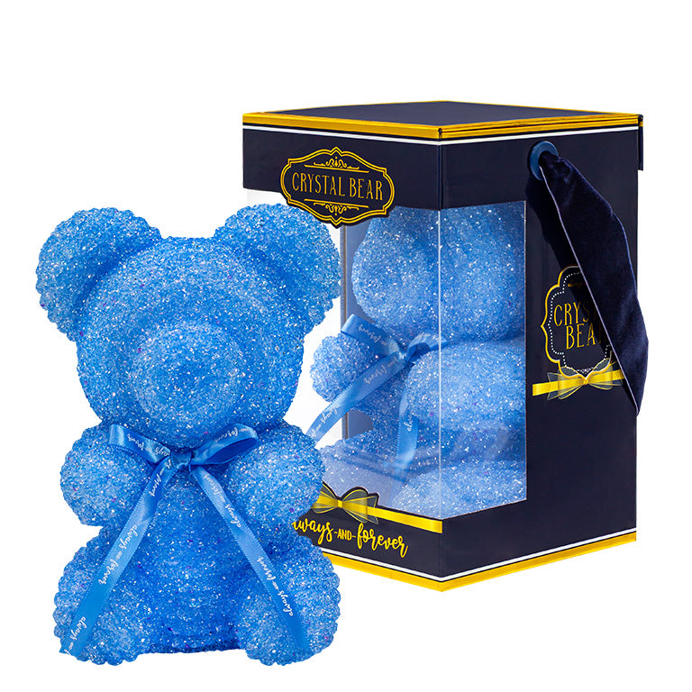 A plastic shaped light blue bear with glitter/crystal aesthic. Behind the bear is the packaging of the product