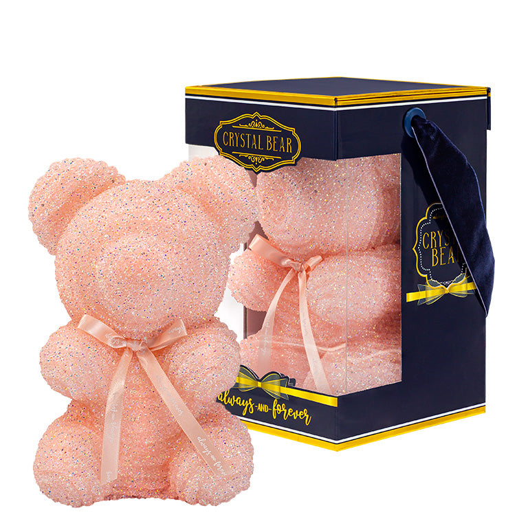 A plastic shaped light pink bear with glitter/crystal aesthic. Behind the bear is the packaging of the product