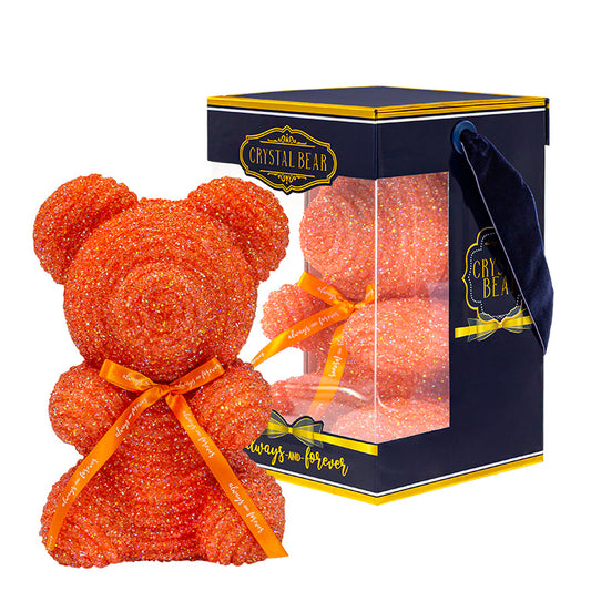 A plastic shaped orange bear with glitter/crystal aesthic. Behind the bear is the packaging of the product