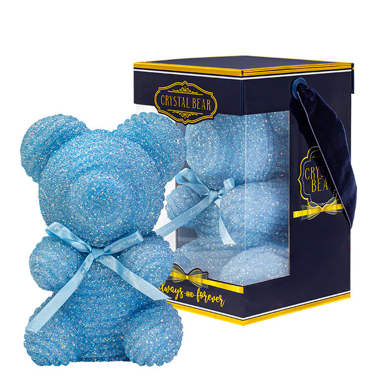 A plastic shaped powder blue bear with glitter/crystal aesthic. Behind the bear is the packaging of the product