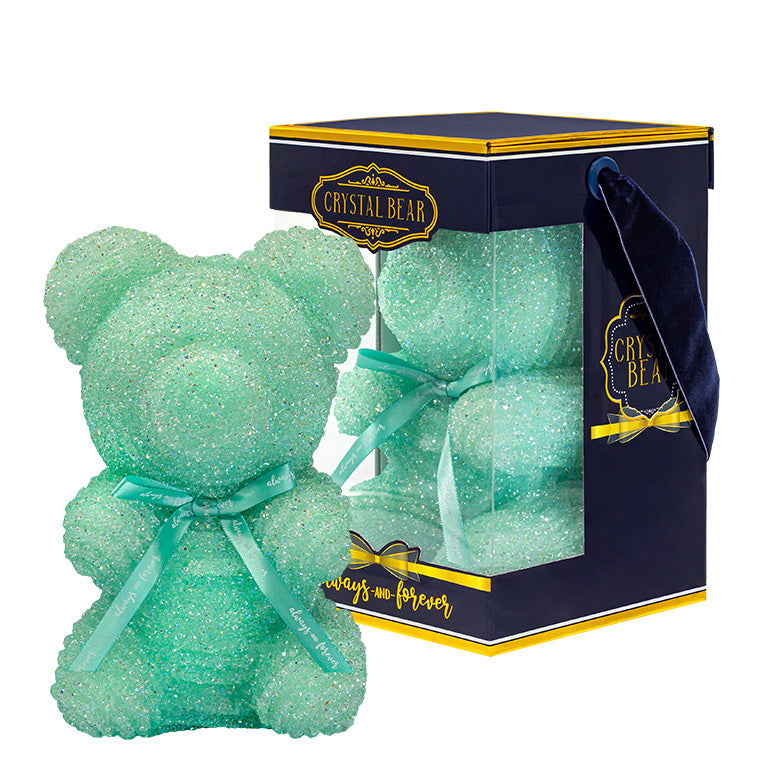 A plastic shaped teal bear with glitter/crystal aesthic. Behind the bear is the packaging of the product