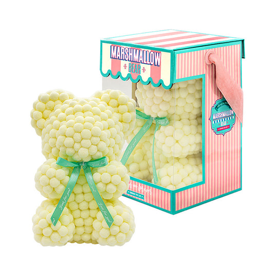 Bear made out of yellow-colored faux marshmallows. The bear is adorned with a green ribbon tied into a bow around its neck, and it is packaged in a clear-front gift box with a pink and white striped design. The top of the box features a teal and pink label that reads "MARSHMALLOW BEAR." This delightful creation is an excellent gift idea for various occasions such as anniversaries, birthdays, graduations, Christmas, Valentine's Day, or simply as a unique gift for someone special.	