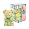 Bear made out of pink, yellow and blue-colored faux marshmallows. The bear is adorned with a green ribbon tied into a bow around its neck, and it is packaged in a clear-front gift box with a pink and white striped design. The top of the box features a teal and pink label that reads "MARSHMALLOW BEAR." This delightful creation is an excellent gift idea for various occasions such as anniversaries, birthdays, graduations, Christmas, Valentine's Day, or simply as a unique gift for someone special.	