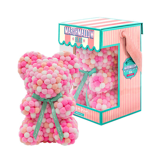 Bear made out of pink, white, peach and pink-colored faux marshmallows. The bear is adorned with a green ribbon tied into a bow around its neck, and it is packaged in a clear-front gift box with a pink and white striped design. The top of the box features a teal and pink label that reads "MARSHMALLOW BEAR." This delightful creation is an excellent gift idea for various occasions such as anniversaries, birthdays, graduations, Christmas, Valentine's Day, or simply as a unique gift for someone special.	