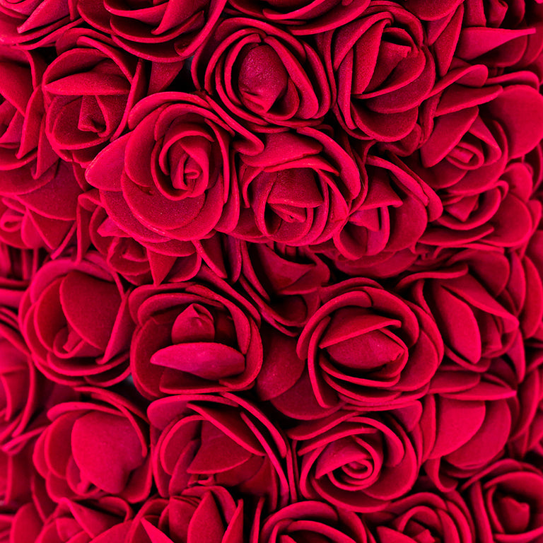 A close up view of the bear shaped product covered in foam roses in the color of burgundy.