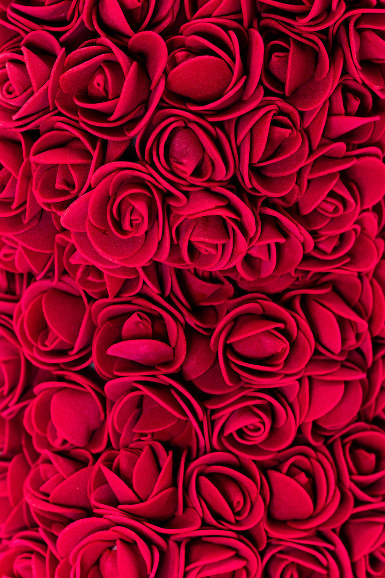 A close up view of the bear shaped product covered in foam roses in the color of burgundy.