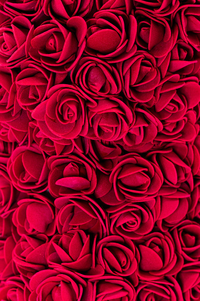 A close up view of the bear shaped product covered in foam roses in the color of red.