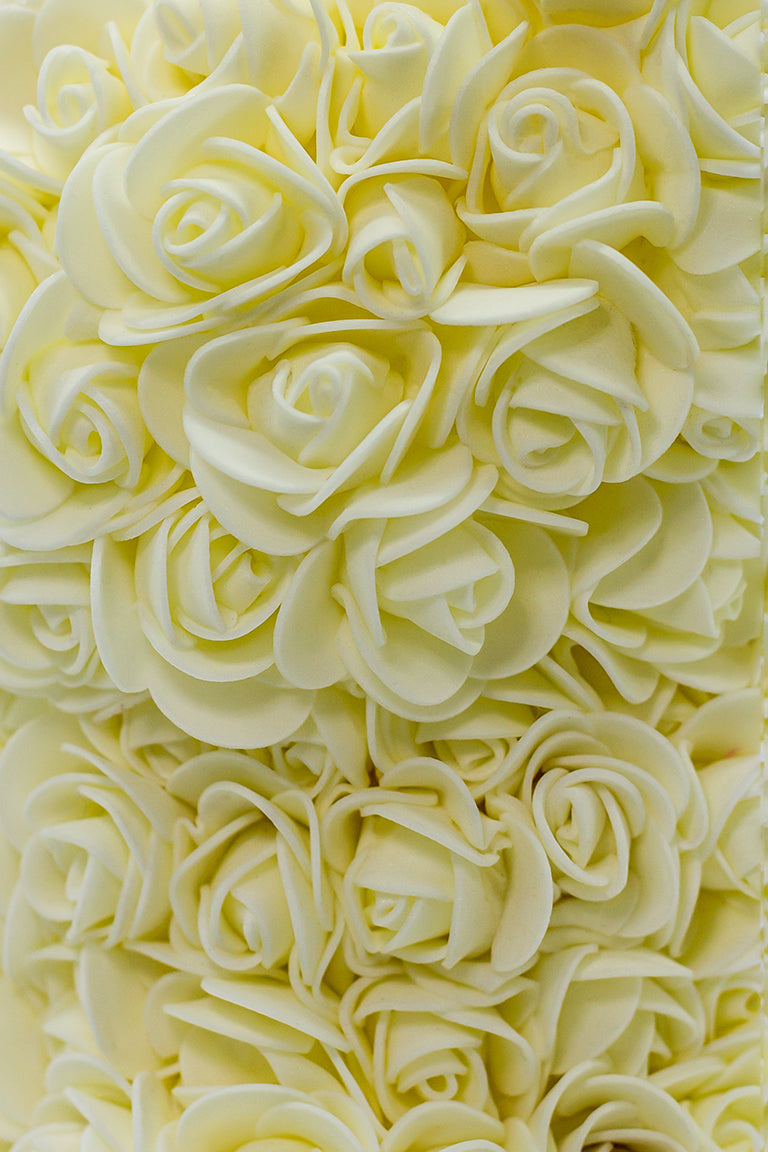 A close up view of the bear shaped product covered in foam roses in the color of cream.
